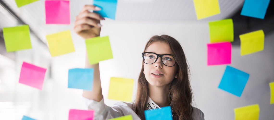 Young girl business woman in glasses watch on transperent wall with a lot of paper stickers on it